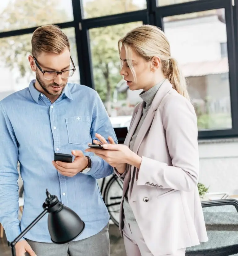 Cntact us 1 young businessman and businesswoman using smartphones together in office 1